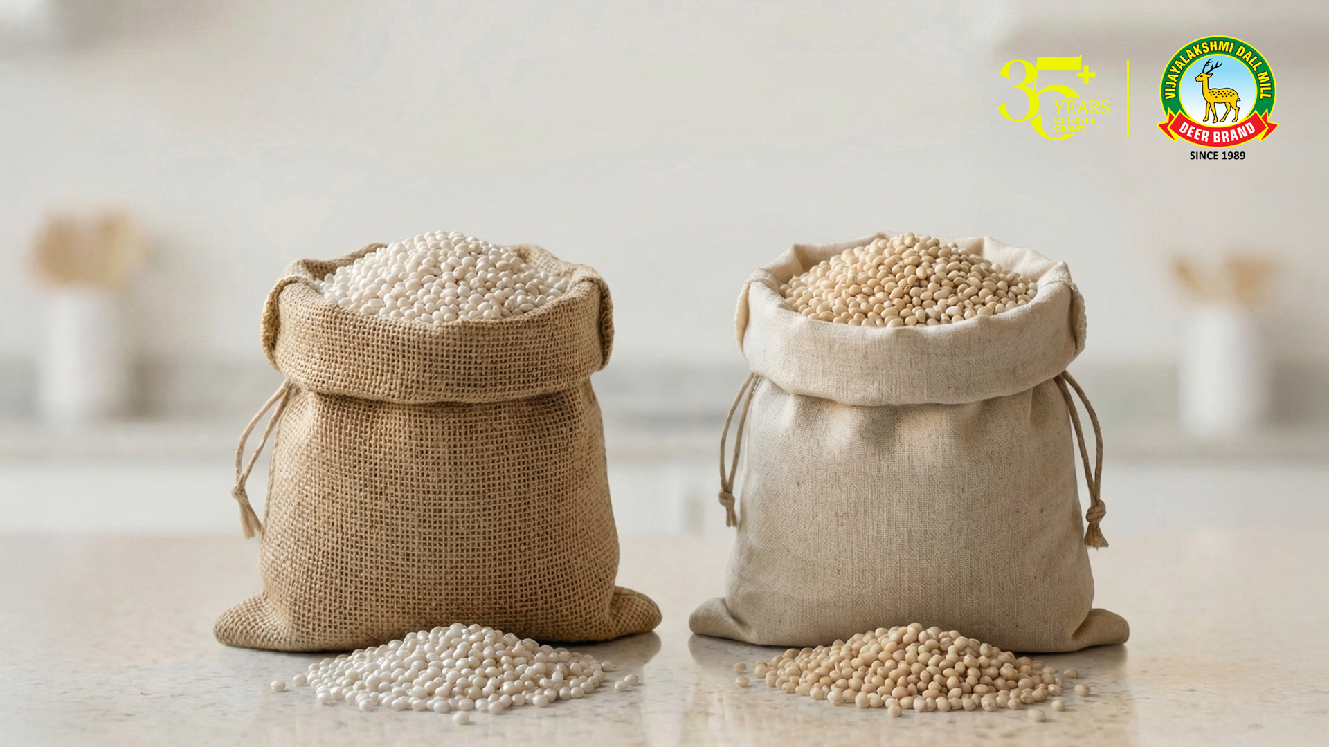 Two burlap sacks filled with white and beige soybeans, with scattered soybeans placed on a light-colored wooden surface. The image also features a logo for Vijayalakshmi Dal Mill Deer Brand, showcasing their 35+ years of quality.